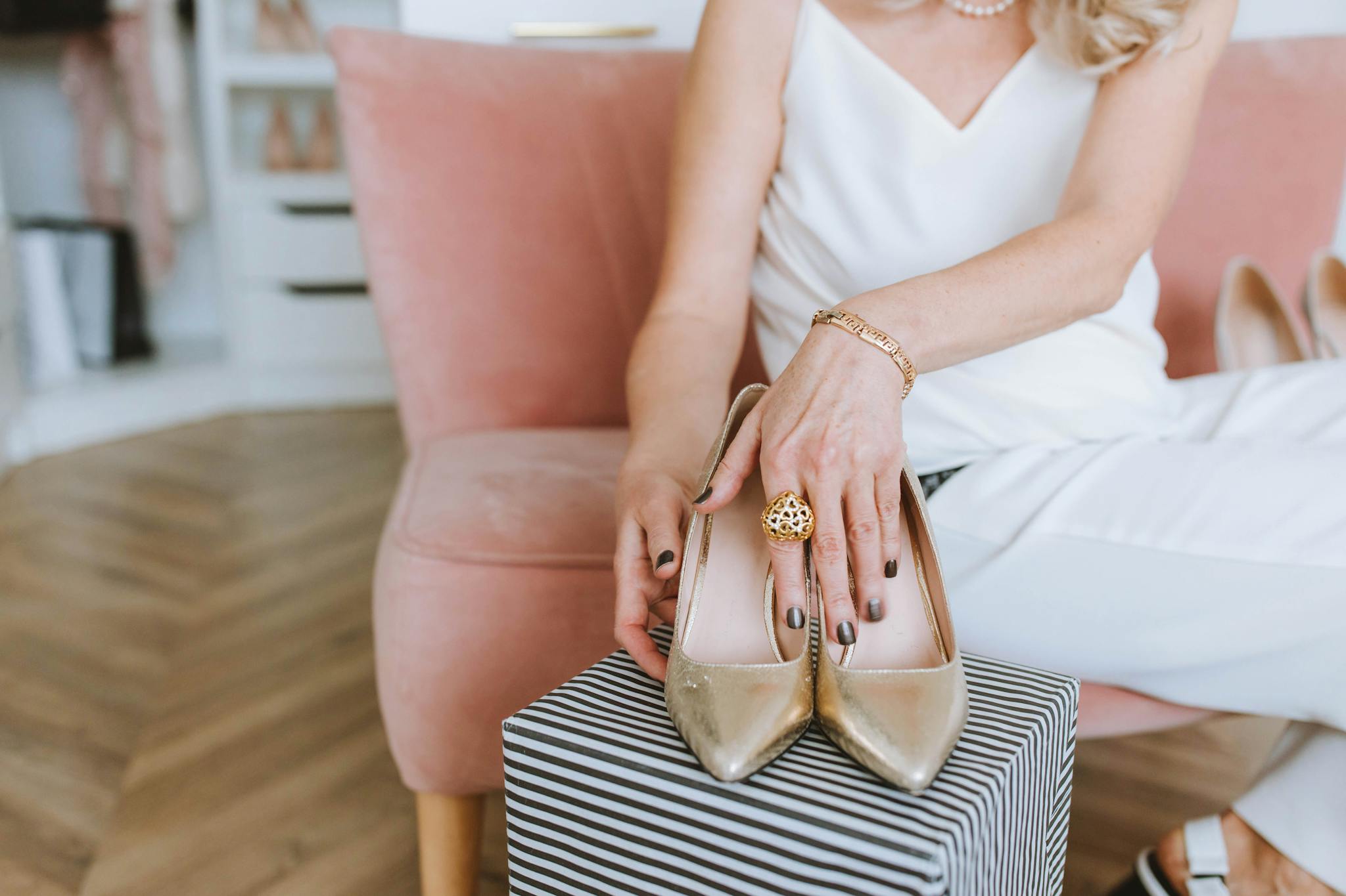 Woman holding gold high heels in a chic, modern room setting.